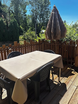 Eine Terrasse aus Holz mit Tisch und Stühlen, umgeben von einem Holzzaun und Bäumen.