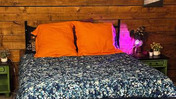 Ein Bett mit einem blumigen Überwurf, zwei Kissen und einem Kopfteil, vor einer Holzwand mit gerahmten Bildern.