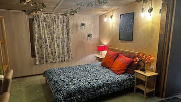 Een slaapkamer met een bed, een nachtkastje, een lamp, een wandlamp en een deur.