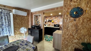 Ein Hotelzimmer mit Bett, Schreibtisch, Ventilator, einer Küchenzeile und einer Wanduhr.
