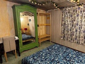 Een kamer met een bed, een groene garderobe, een houten stapelbed, een bureau met stoel en een kamerbreed gordijn met dessin.