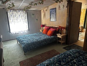 A bedroom with a bed, bedside tables, a nightstand, a window with curtains, and a wall-mounted picture.