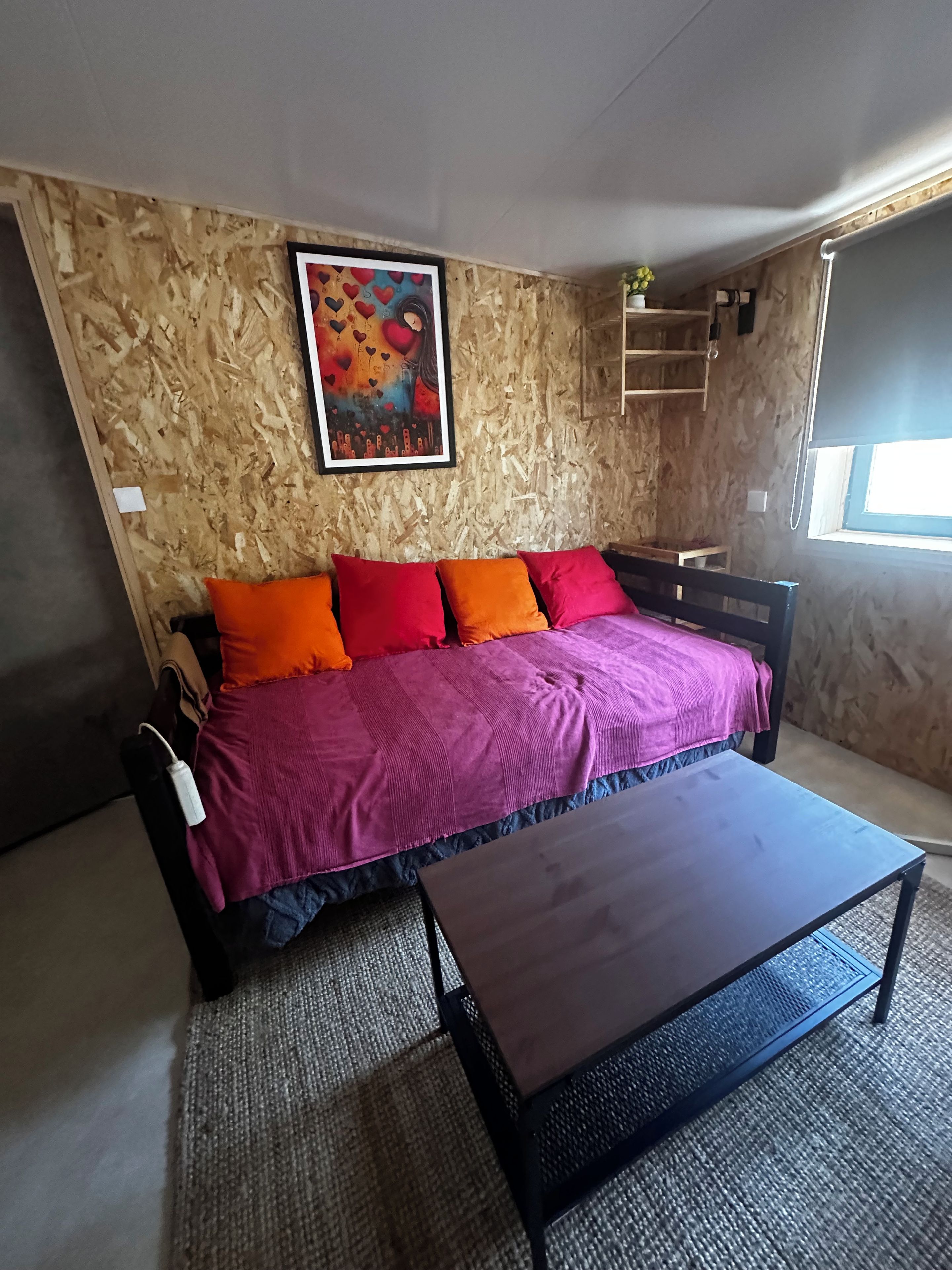 Quarto com cama, mesa de centro, pintura na parede e janela.
