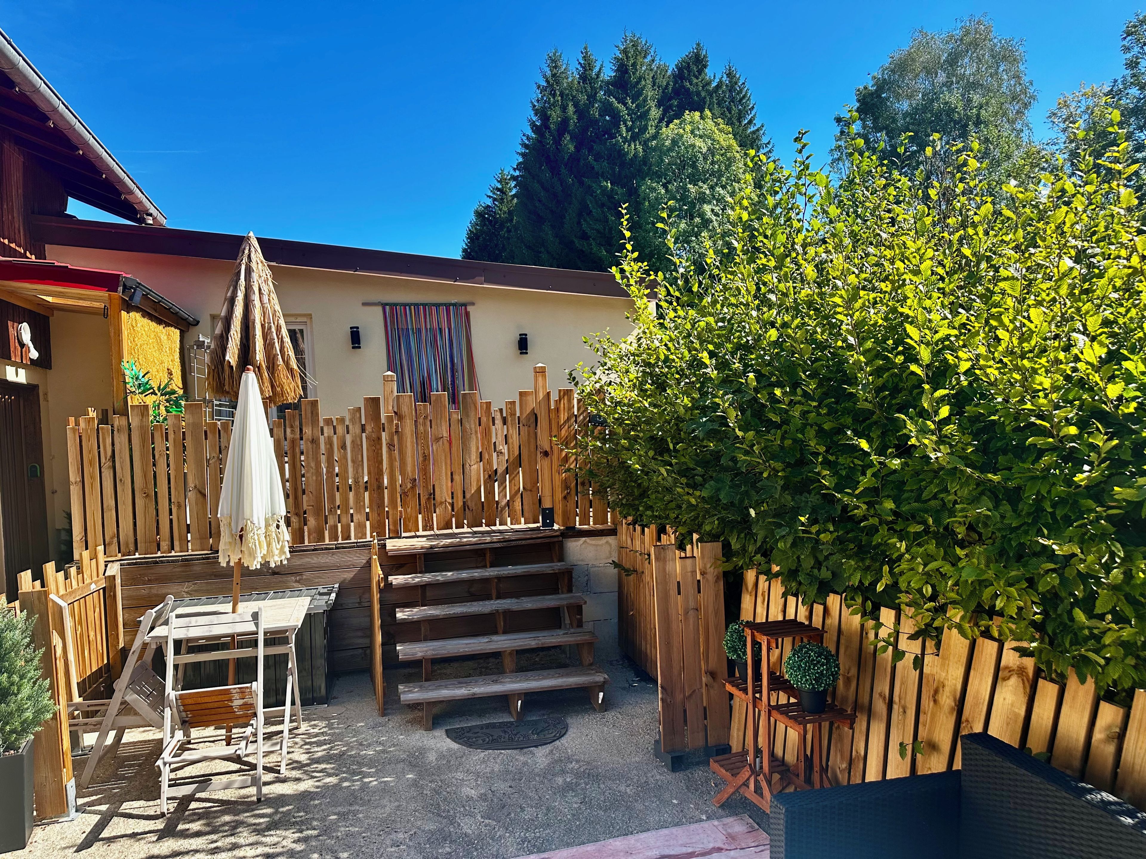 A wooden deck with a table and benches, surrounded by a wooden fence and a large bush.