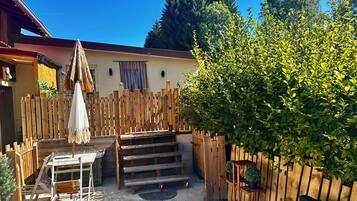 A wooden deck with a table and benches, surrounded by a wooden fence and a large bush.