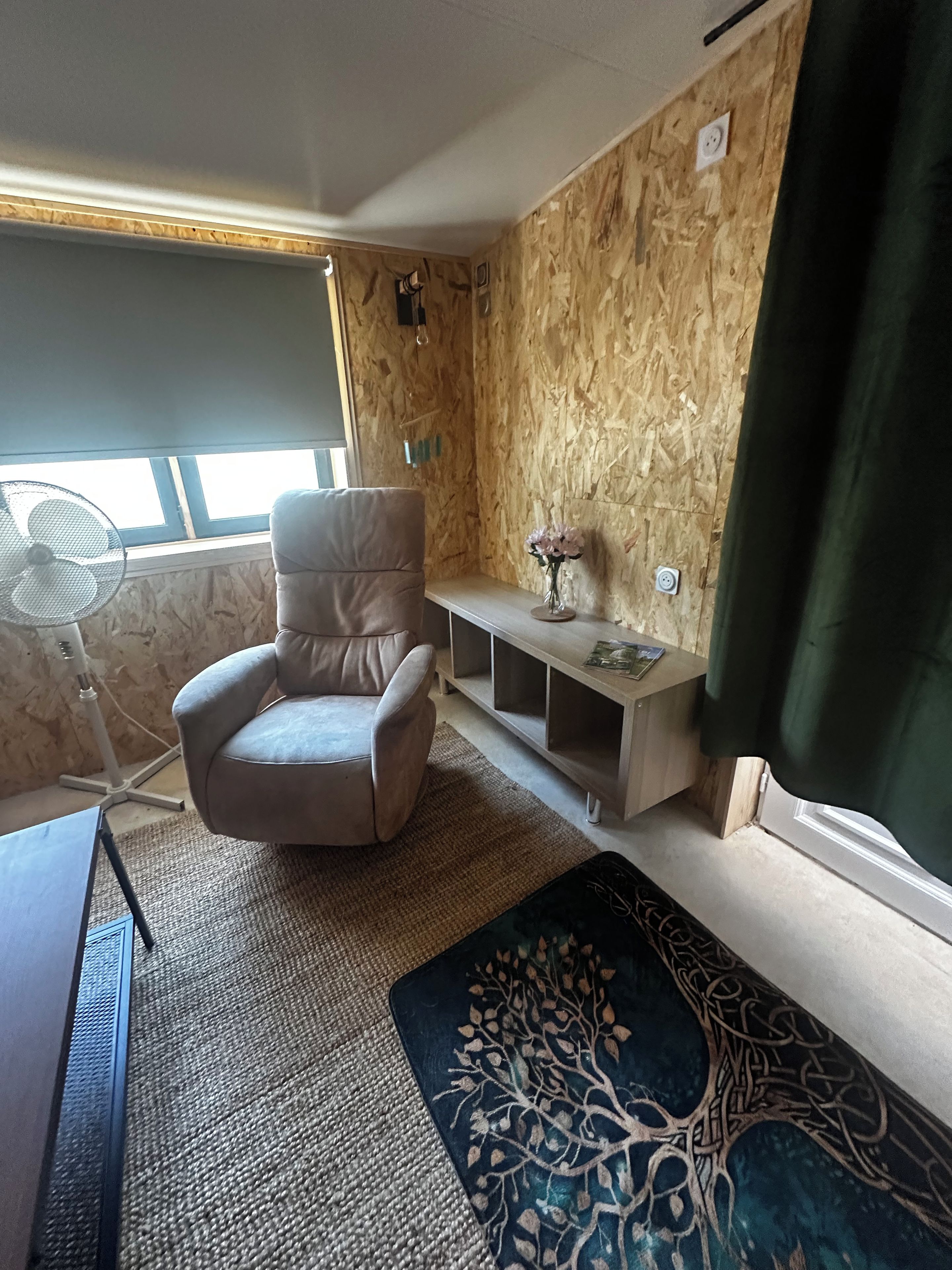 A room with a chair, a small table, a fan, and a window.
