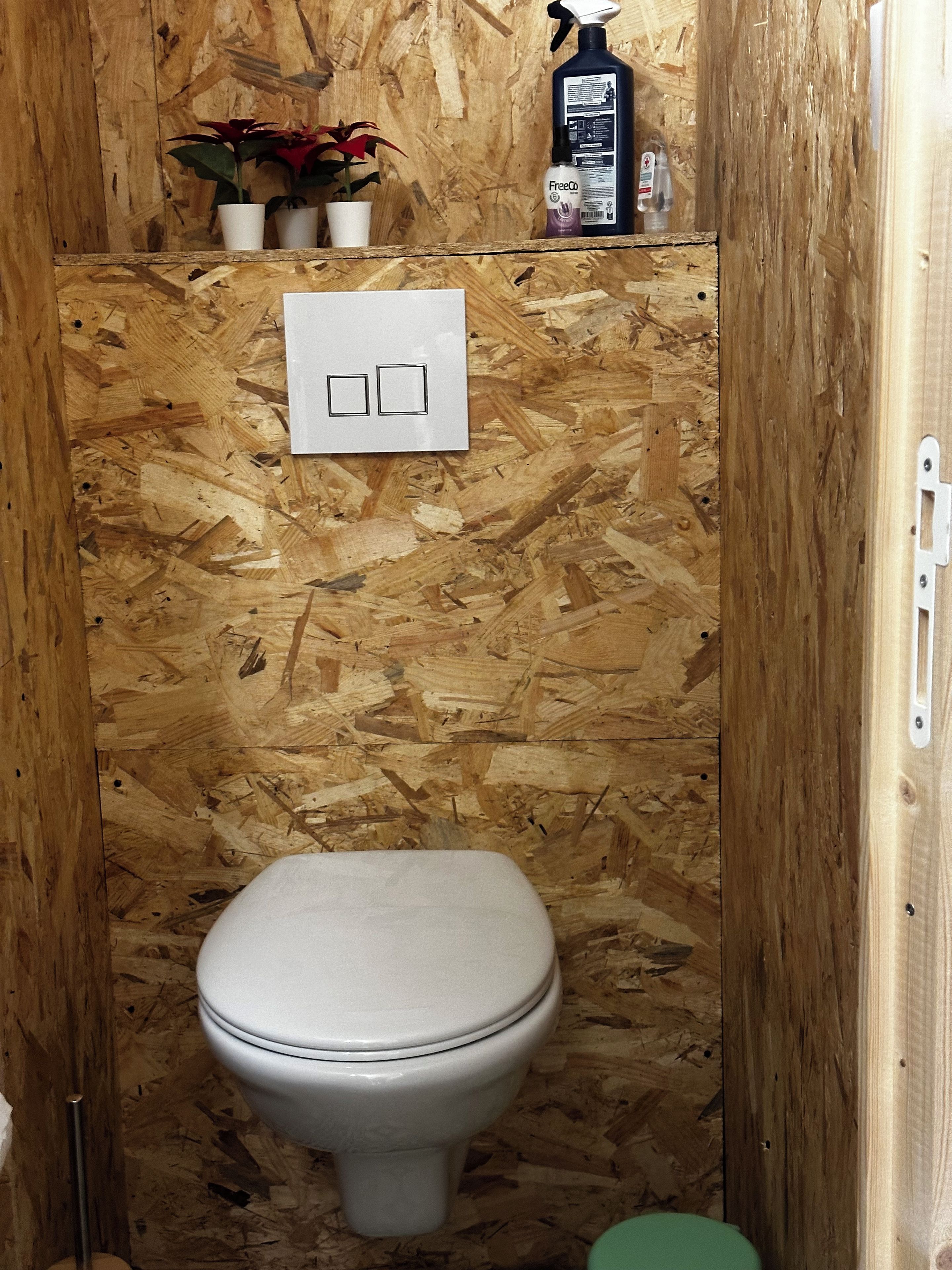 Een kleine badkamer met houten lambrisering, een toilet, een wit bedieningspaneel en een plant.