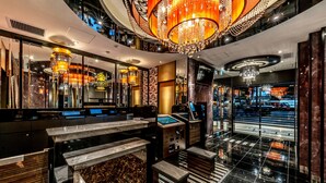 A luxurious hotel lobby with a marble reception desk, a large chandelier, and a modern design.