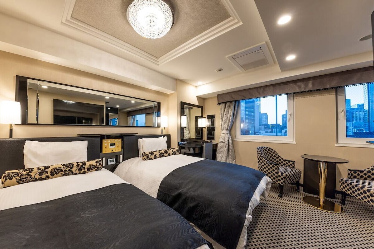 A hotel room with two beds, a large mirror, a city view, a desk, and a chair.
