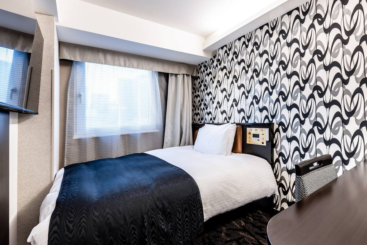 A hotel room with a bed, a TV, a control panel, and a patterned wall.