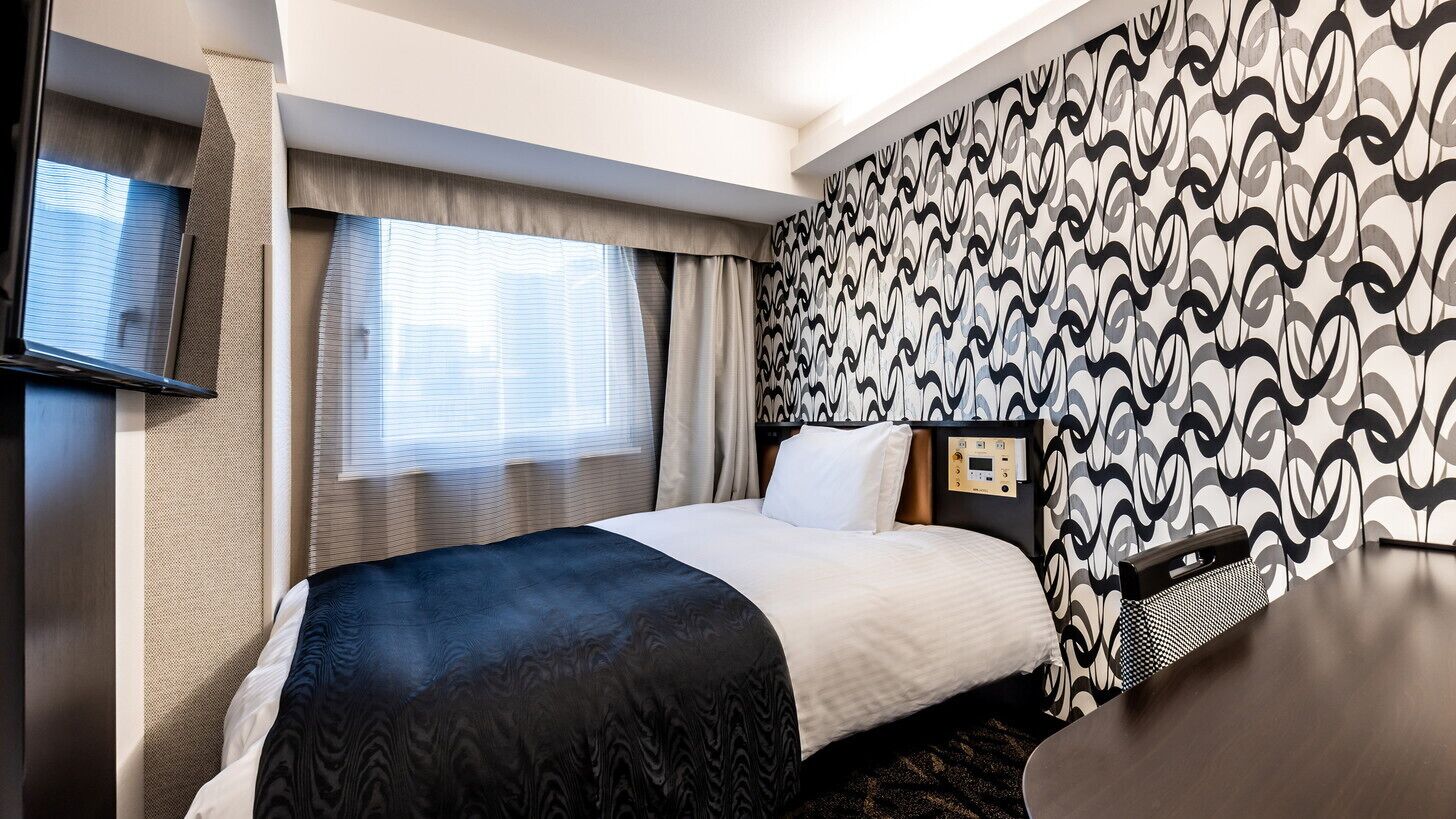 A hotel room with a bed, a TV, a bedside table, and a patterned wall.