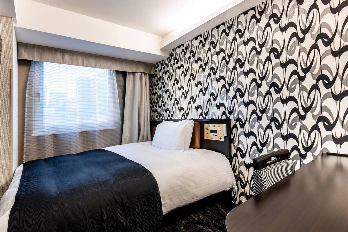 A hotel room with a bed, a TV, a bedside table, and a patterned wall.