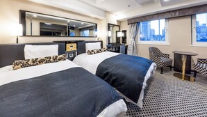 A hotel room with two beds, a desk, a chair, a small table, and a large window with a city view.