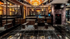 A modern hotel lobby with a central chandelier, marble flooring, and a reception desk.