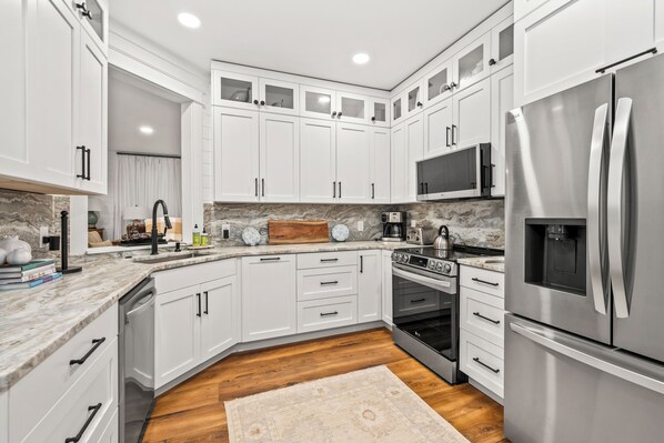 A modern kitchen with white cabinetry, stainless steel appliances, a marble countertop, and a wooden floor.