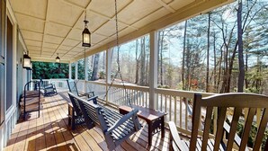 Une terrasse en bois avec des sièges extérieurs, une rambarde et une vue sur une zone boisée.