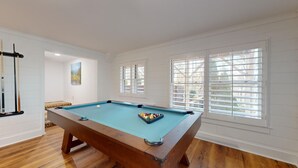 Une table de billard dans une pièce aux murs blancs et au plancher en bois.