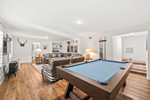 A pool table in a well-lit room with a wooden floor, a sofa, and a fireplace.