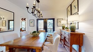 A dining room with a wooden table, white chairs, a chandelier, and a view through a glass door. - Lake Views, a Pool Table, and a Porch Swing. The Perfect Mountain Trip | Lakeview Hideaway (Highlands)