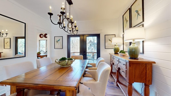 Ein Esszimmer mit Holztisch, weißen Stühlen, einer Chandelüster und Blick durch eine Glastür.