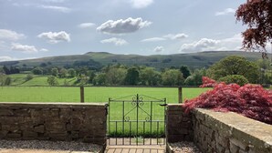 A stone pathway leading to a metal gate, surrounded by stone walls and a green field.