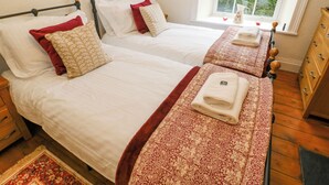 A hotel room with two beds, each with white linens and red and beige patterned pillows. There is a window with a view of greenery outside.