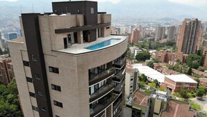 A high-rise building with a rooftop pool, multiple balconies, and a view of a cityscape with other buildings.