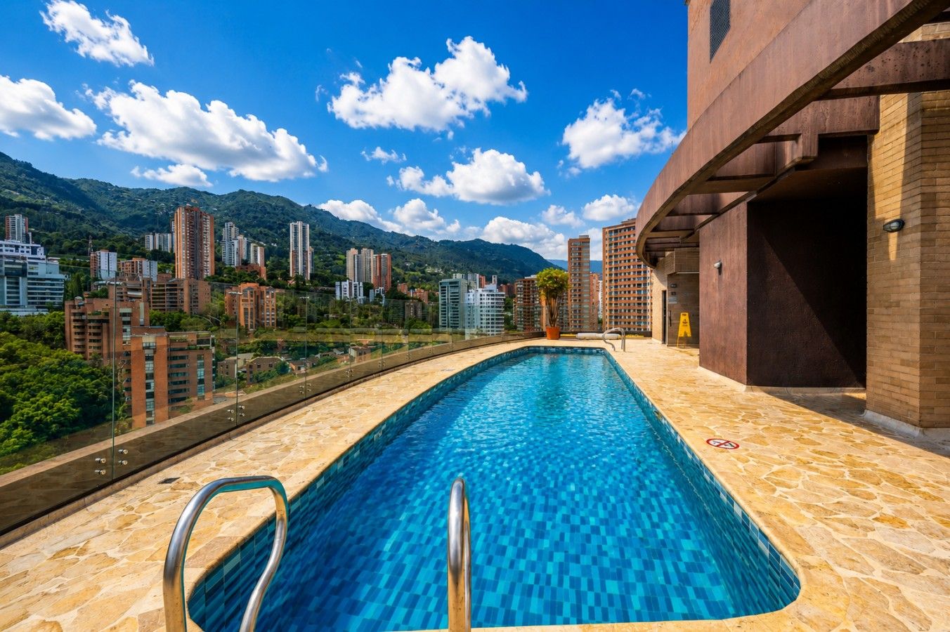 A rooftop swimming pool with a clear view of surrounding high-rise buildings and mountains.
