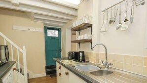 Une cuisine équipée d’un évier, d’un plan de travail et d’un grille-pain. On y trouve une porte avec une fenêtre, ainsi qu’une étagère avec des tasses et des ustensiles.