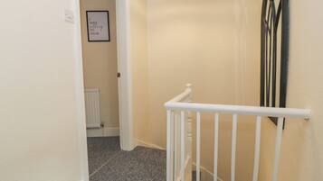 A staircase with a white handrail and a black balustrade, leading to a room with a radiator and a framed quote on the wall.