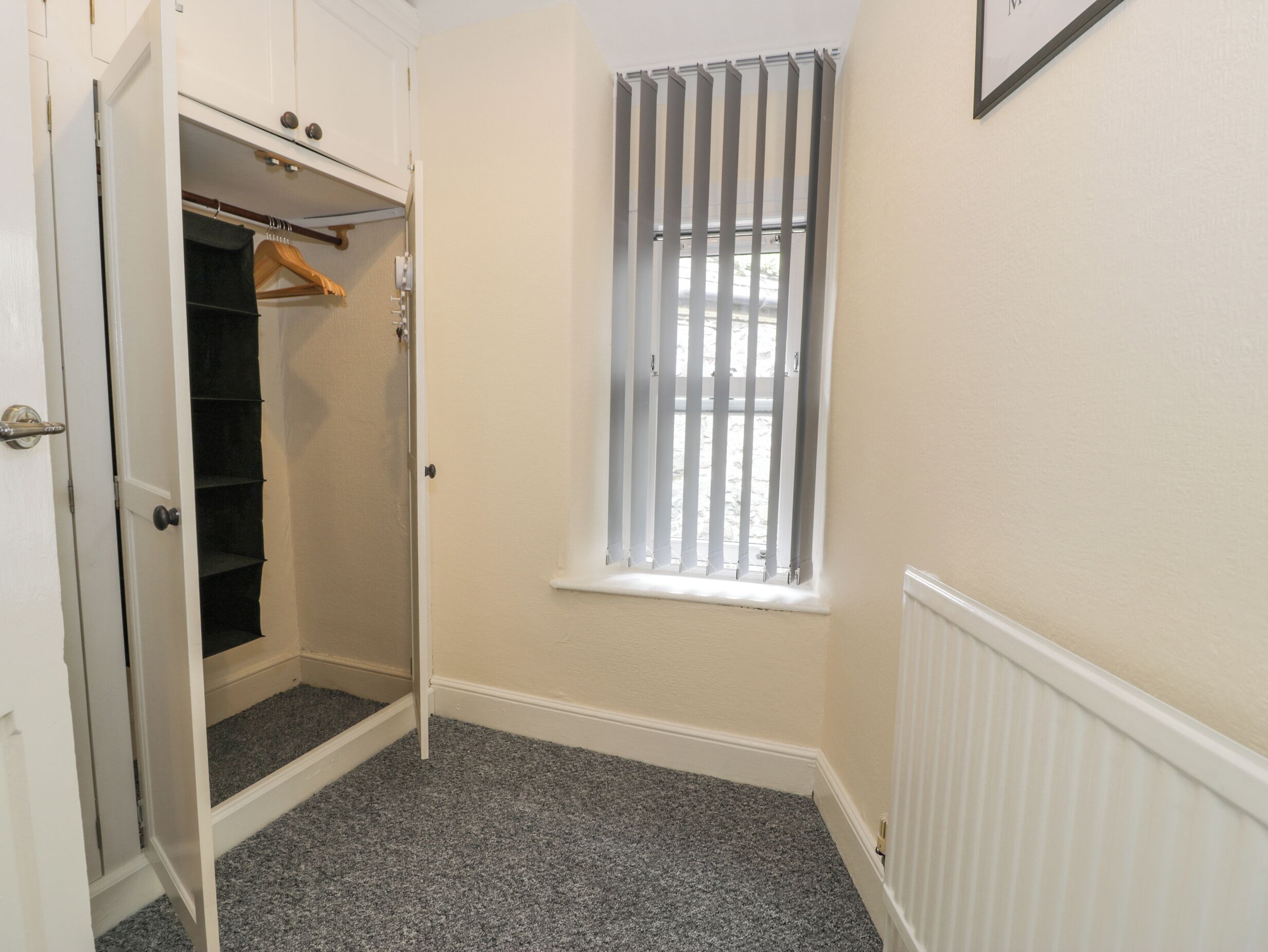 A room with a walk-in closet, a window with vertical blinds, and a radiator on the wall.