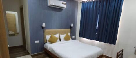 A hotel room with a bed, a desk, a chair, a ceiling fan, and an air conditioning unit.