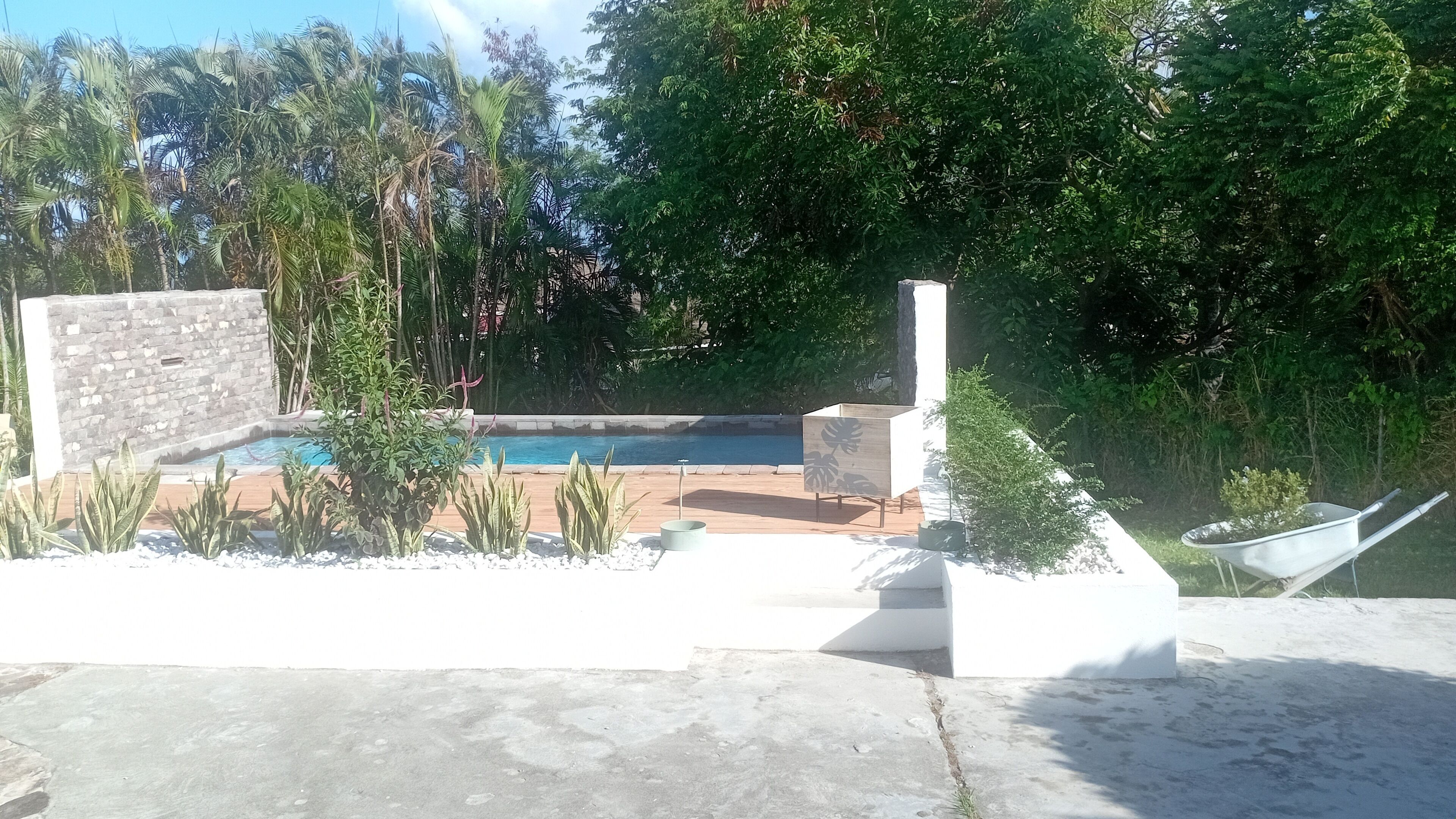 Una piscina rodeada por un muro de piedra, con una terraza de madera y una jardinera.