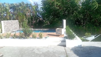 Una piscina rodeada por un muro de piedra, con una terraza de madera y una jardinera.