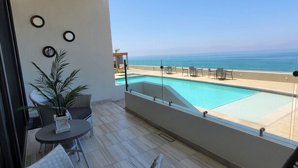 A balcony with a pool, chairs, and a potted plant. - Seafront Luxury Seaside Condo + Pool & Jacuzzi (Rosarito)