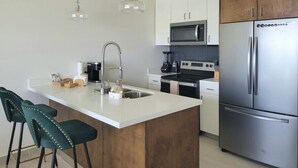 A modern kitchen with a central island, stainless steel appliances, and wooden cabinetry. - Seafront Luxury Seaside Condo + Pool & Jacuzzi (Rosarito)