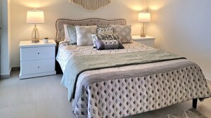 A bedroom with a bed, two bedside tables, and a macrame wall hanging. - Seafront Luxury Seaside Condo + Pool & Jacuzzi (Rosarito)