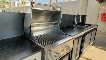 An outdoor kitchen with a grill, sink, and storage cabinets.