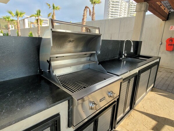 Une cuisine extérieure équipée d’un barbecue, d’un évier et de meubles de rangement.
