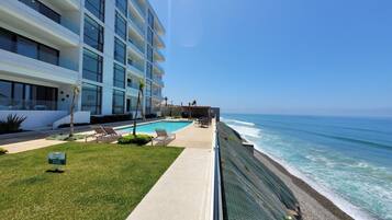 A hotel with a pool, a beach view, and a clear sky.