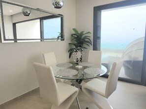 Un espace repas moderne avec une table en verre entourée de chaises blanches, un élément décoratif central et un grand miroir au-dessus.