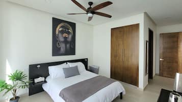 A modern bedroom with a large bed, a ceiling fan, a wooden wardrobe, and a potted plant.