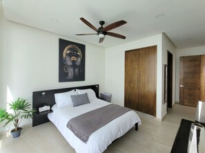 Une chambre à coucher moderne avec un grand lit, un ventilateur de plafond, une armoire en bois et une plante en pot.