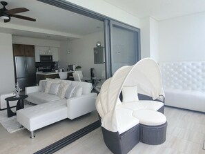 Un salon moderne avec un canapé d’angle, un fauteuil blanc et un banc rembourré.