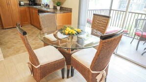 A dining area with wicker chairs and a glass table, featuring a fruit centerpiece.