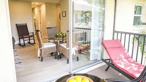 A balcony with wicker furniture, a glass door, and a red lounge chair.