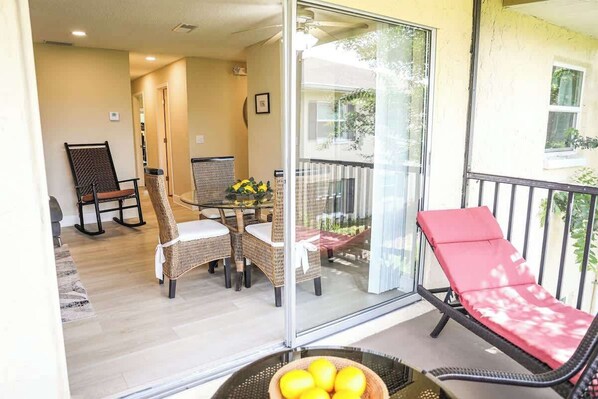 A balcony with wicker furniture, a glass door, and a red lounge chair.