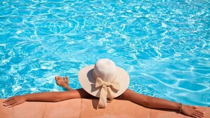 A person relaxing on a sun lounger by a clear blue pool.