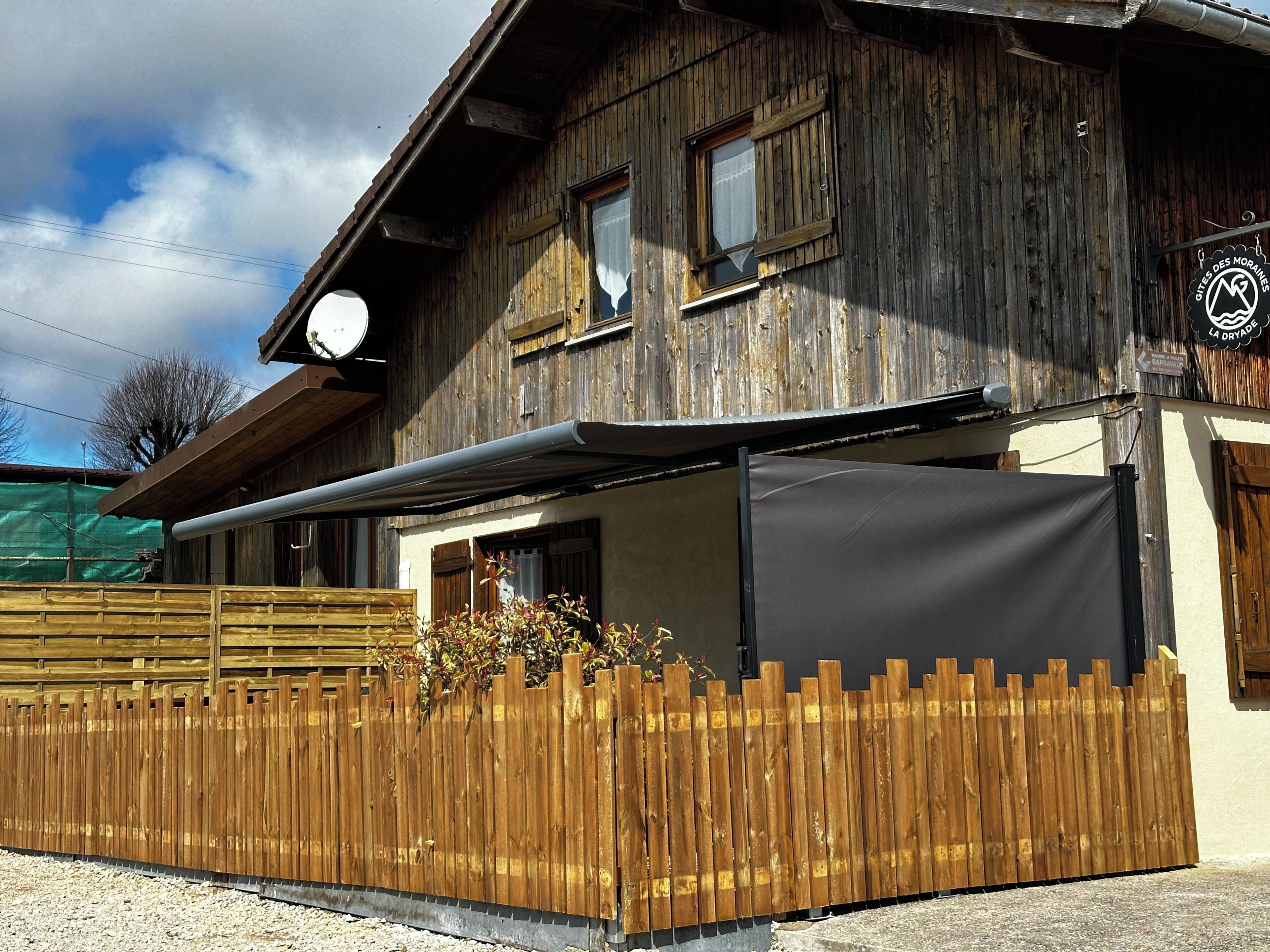 Een landelijk houten gebouw met een overdekte patio, een houten omheining en een bordje met de naam Dryade restaurant.