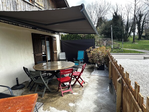 An outdoor patio with a round table, chairs, and a covered area. - Chalet 8 à 10 Personnes (Monnet-la-ville)